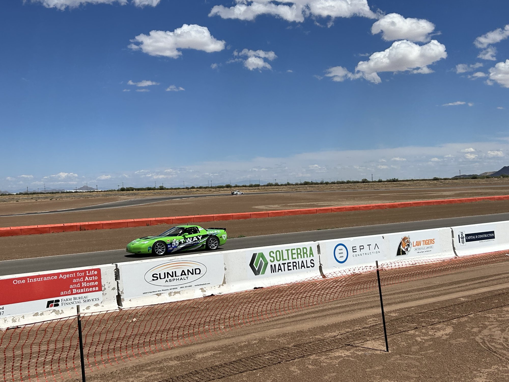 Green #55 C5 Corvette on a desert track behind sponsor barriers