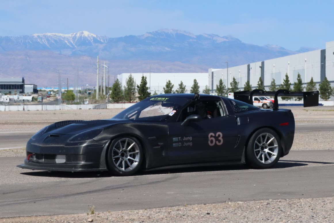 Gunmetal #63 C6 Corvette Z06 exiting a corner with mountains behind