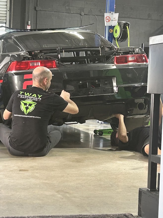 Two mechanics working under the rear of a black race car