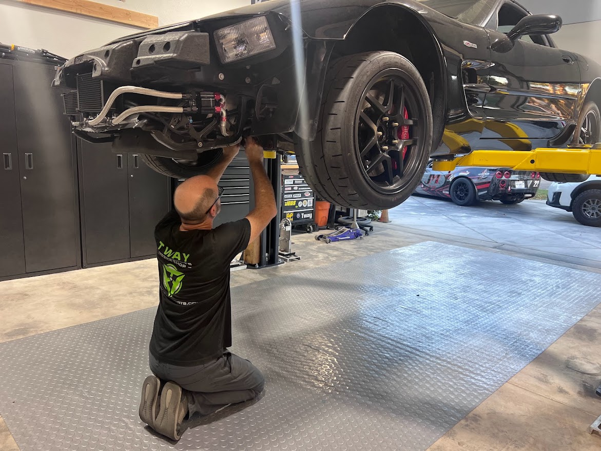 Mechanic working under a lifted black car in the shop